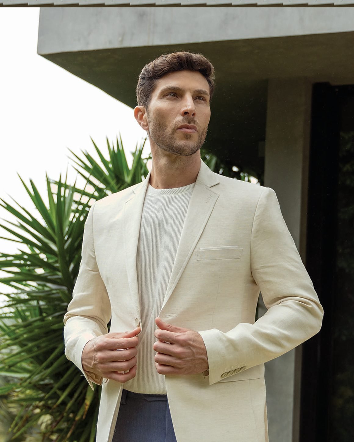 Blazer creme sobre camiseta branca, em fachada de concreto