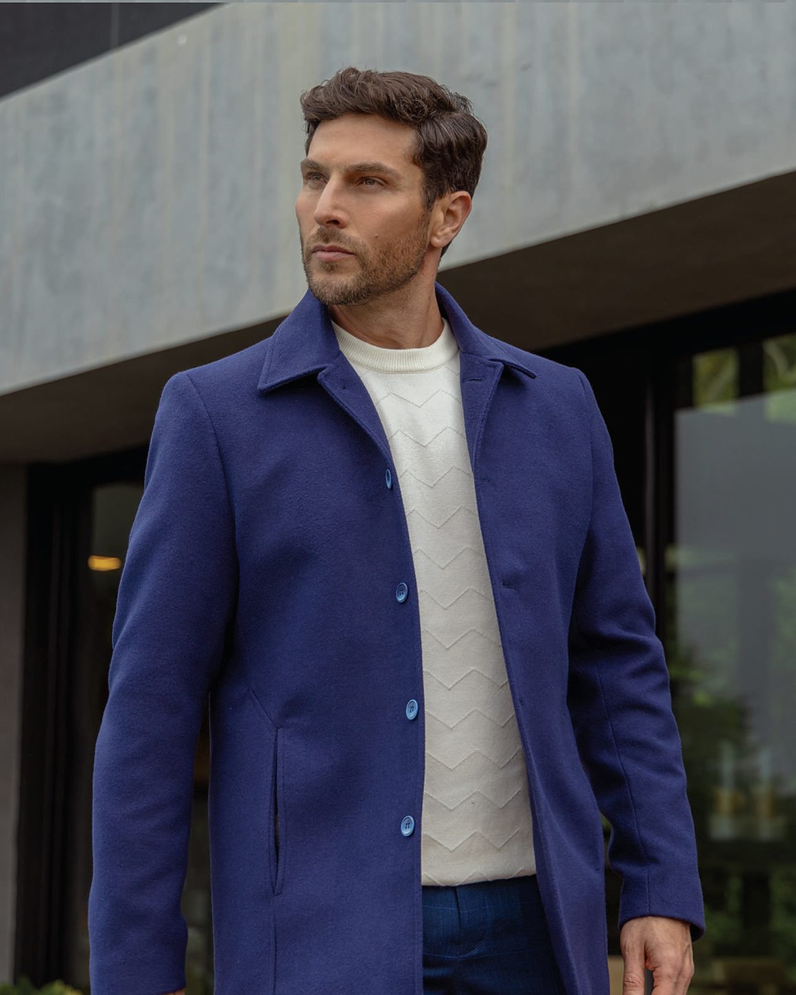 Sobretudo azul royal sobre camisola bege, em ambiente externo