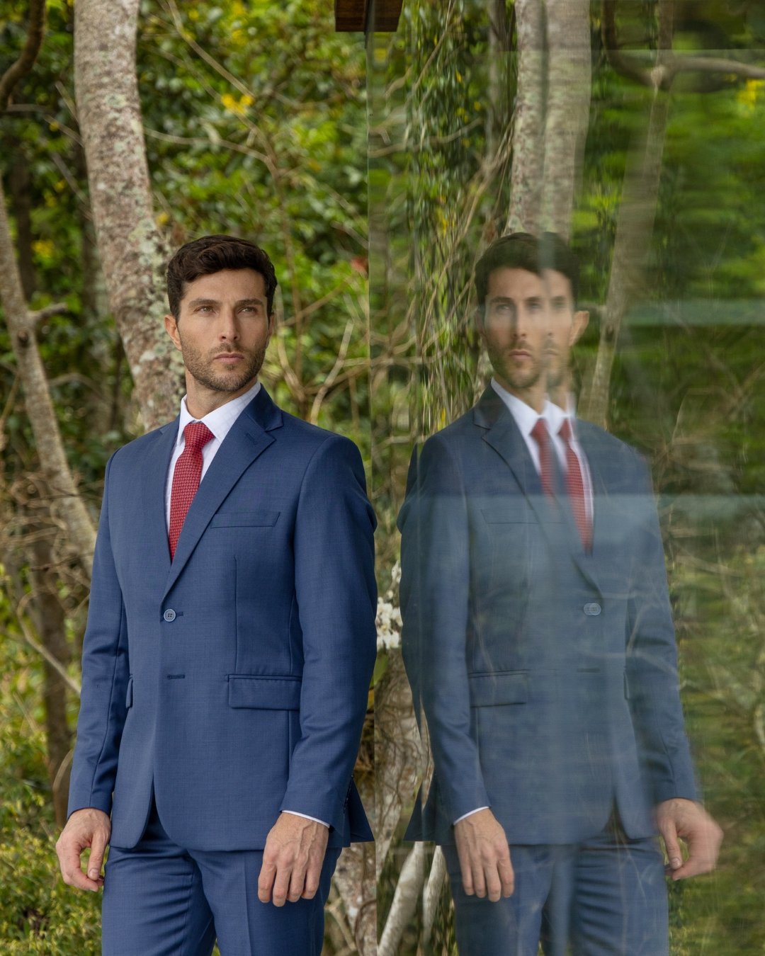 Terno azul refletido em painel de vidro, com vegetação ao redor